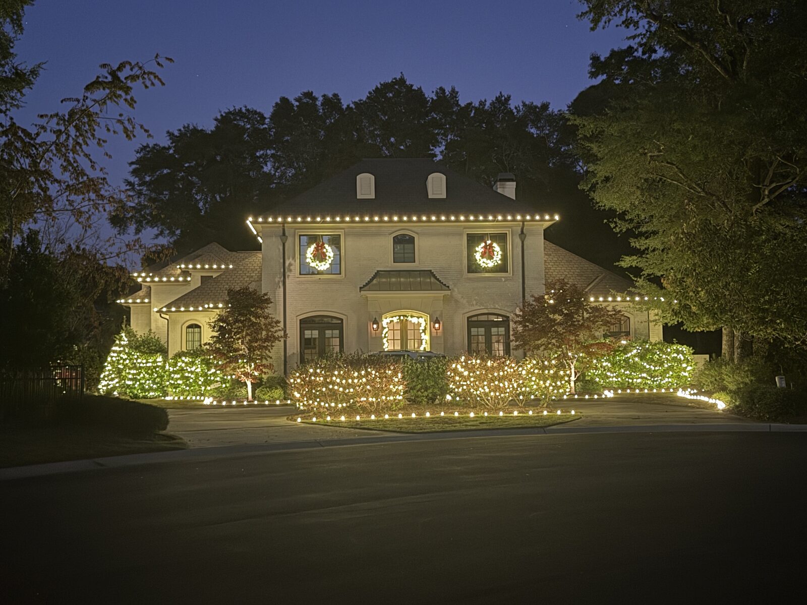 Two-story home outlined in warm white Christmas lights with lit wreaths